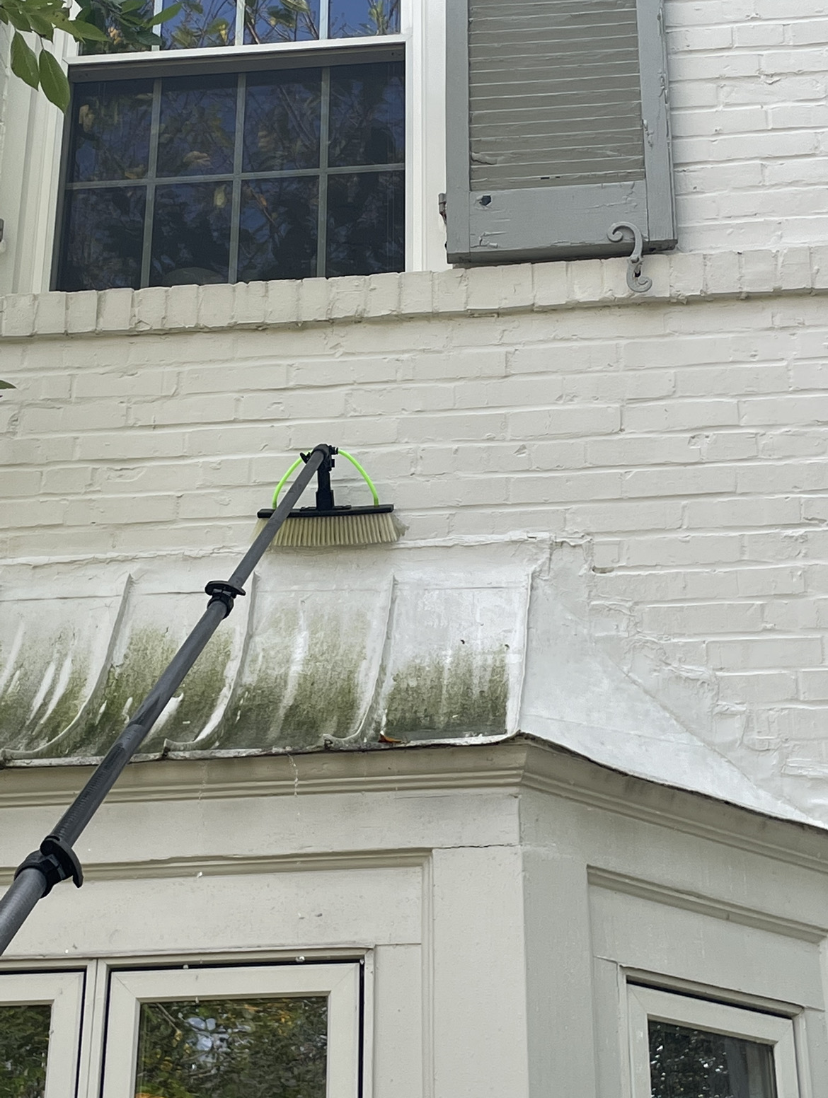 Bay-window roof flashing covered in green algae streaks before soft wash