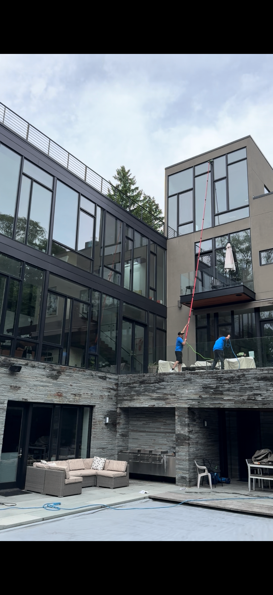 Modern home with crew using water-fed poles to clean upper windows from a terrace